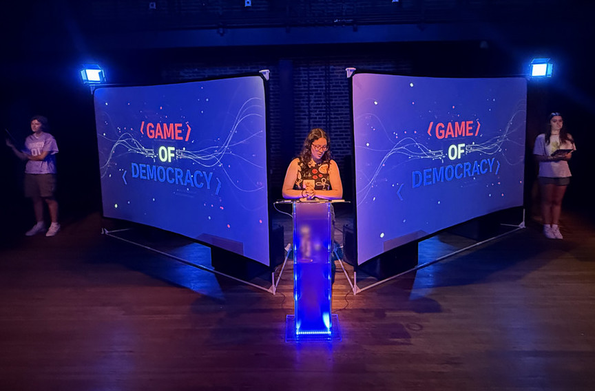 A woman standing at a podium between 2 screens with the words Central Memory Processing Unit on them