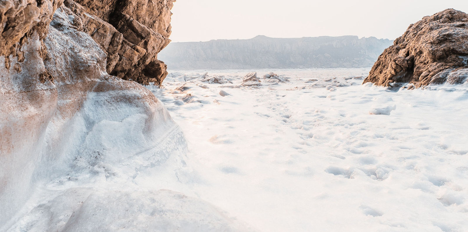 Standing on the surface of a glacier, between two rocky formations, with a cliff in the distance.