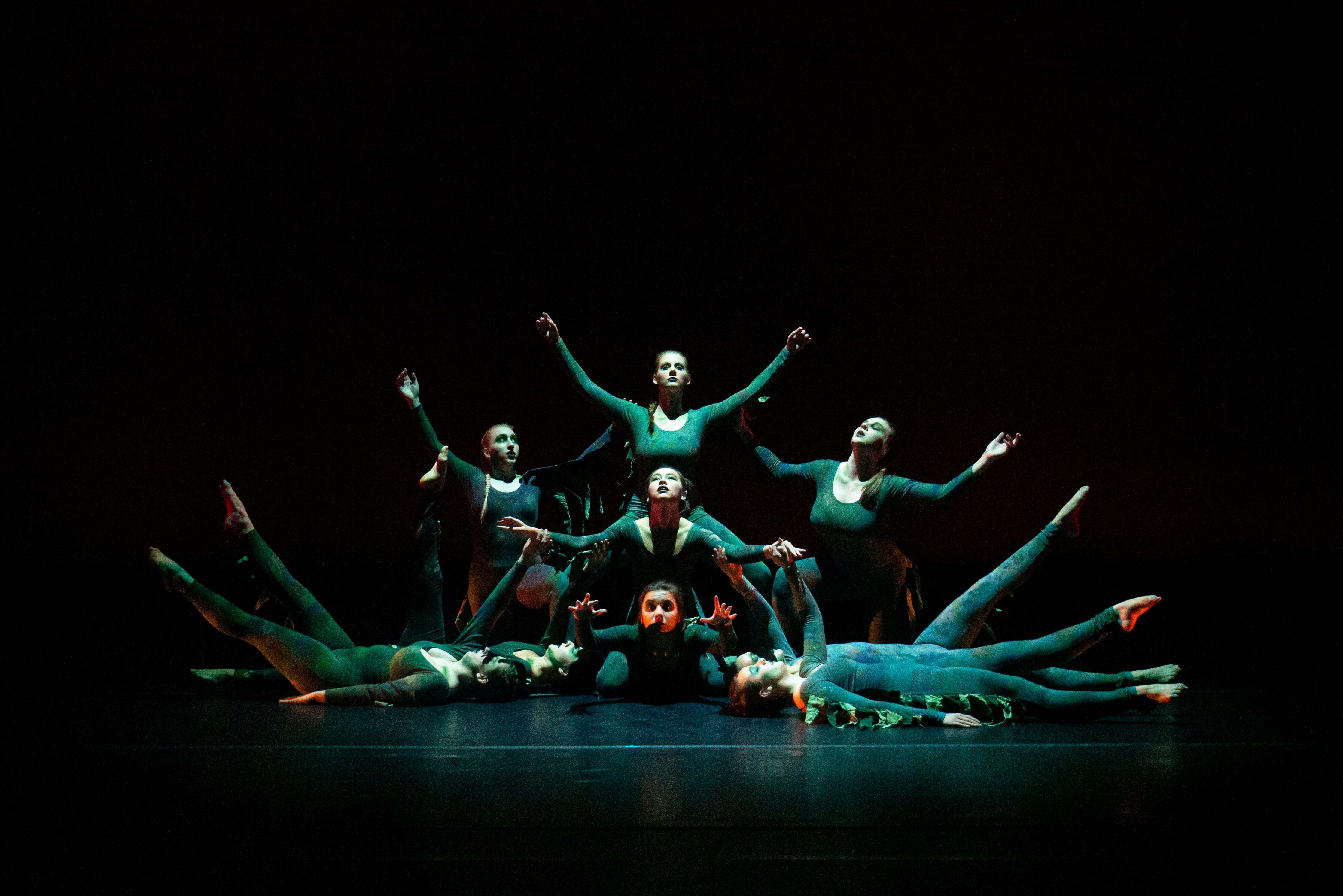 Dancers are in a V formation. Four dancers are standing in the center of the image in various poses.