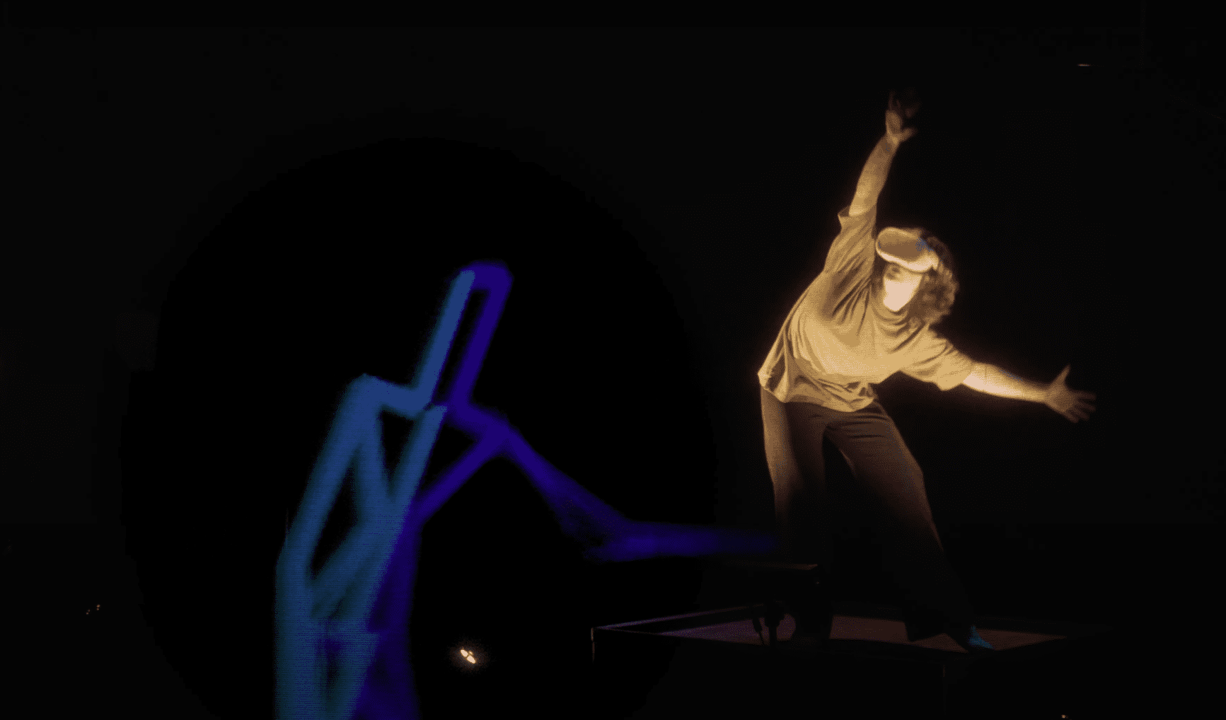 Dancer standing in a room with a VR headset on with a projected image of a person in behind the dancer.