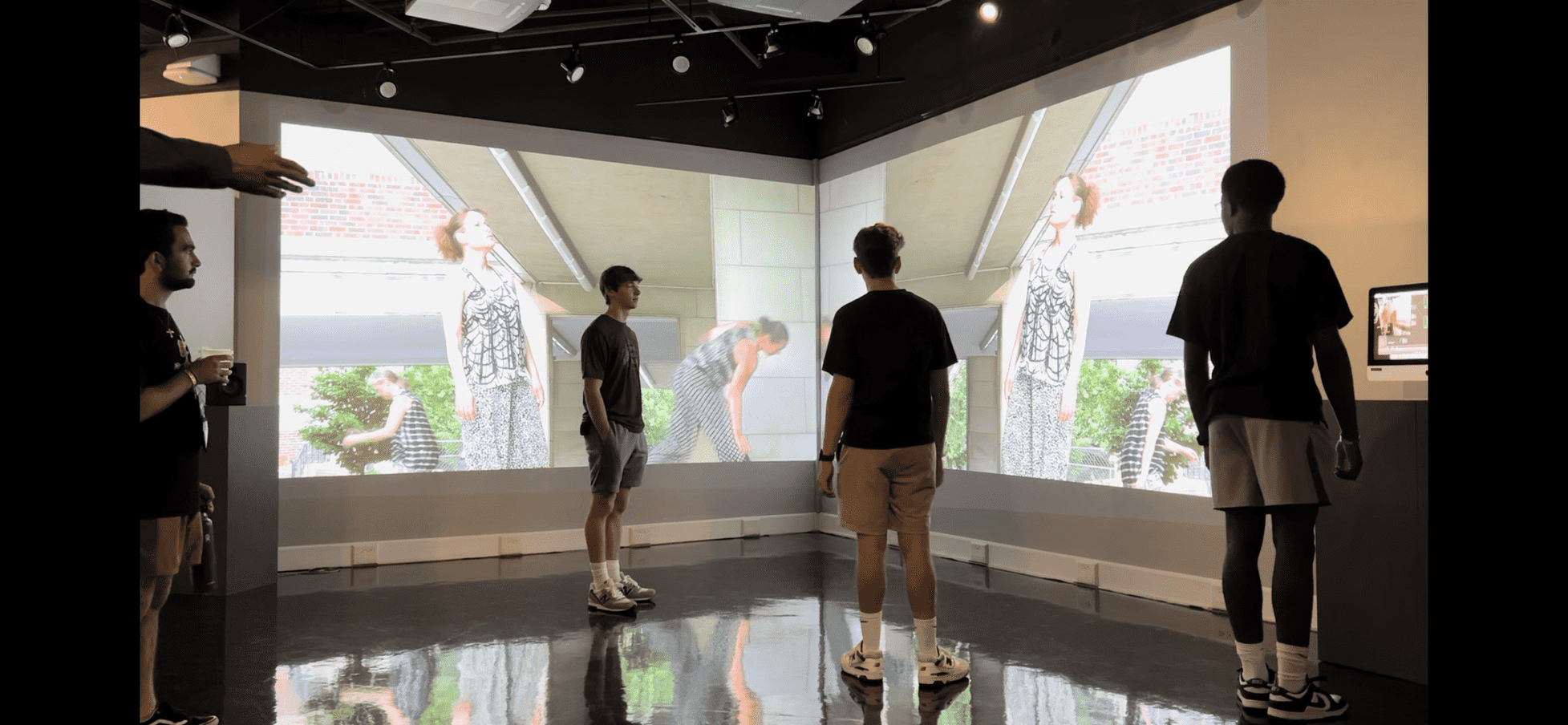Students standing in a room with projection screens in front of them.