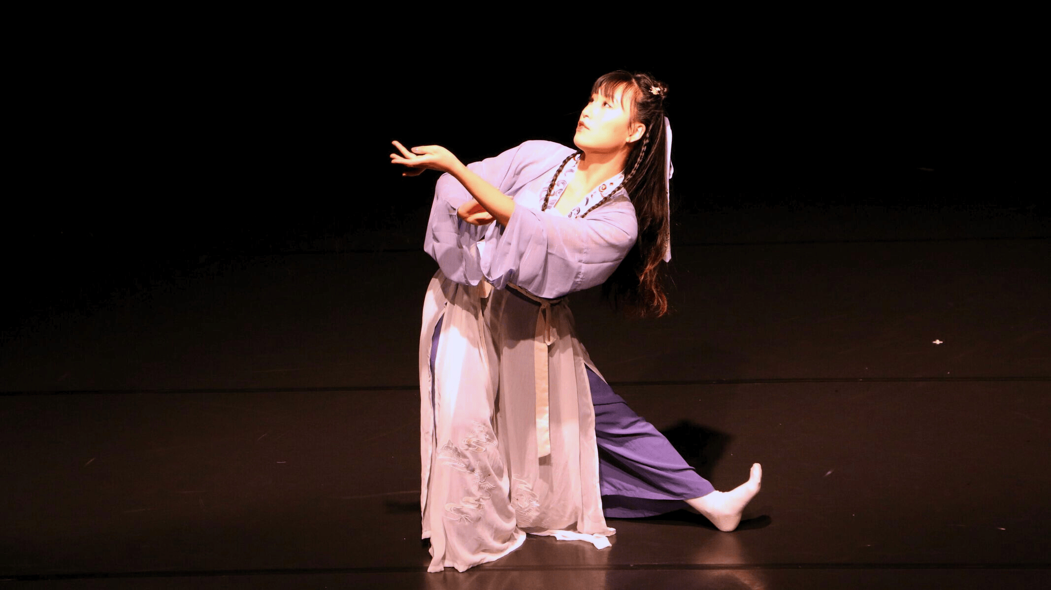 Single dancer on stage dressed in traditional Asian clothing posed at an angle.