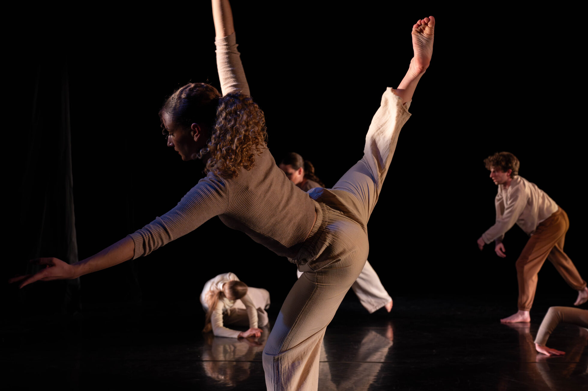 Solo dancer on stage reach arms forward and a leg in back attitude.