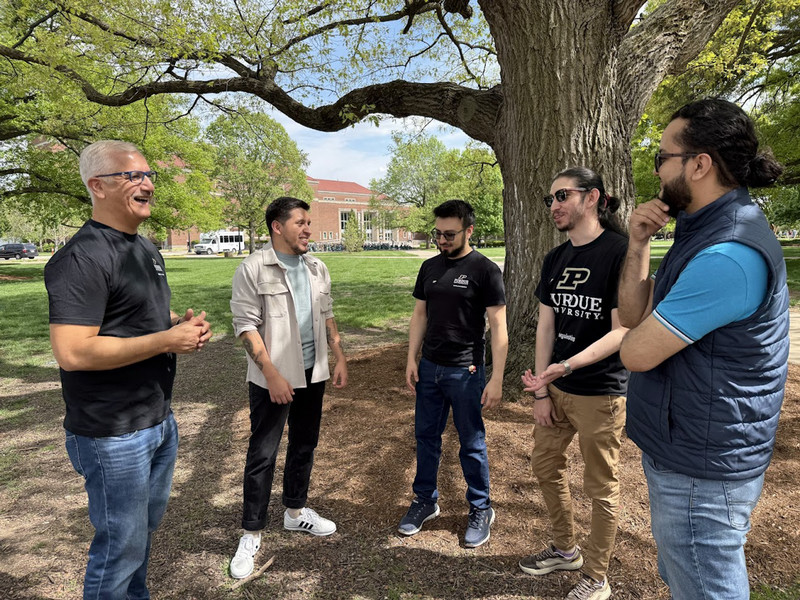 five people students and faculty standing outside laughing near a tree