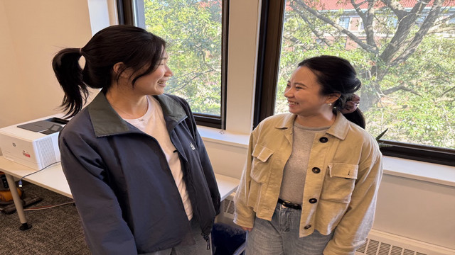 two students smiling and talking to each other in a room 