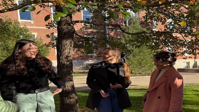 Three students standing outside by a tree laughing. 