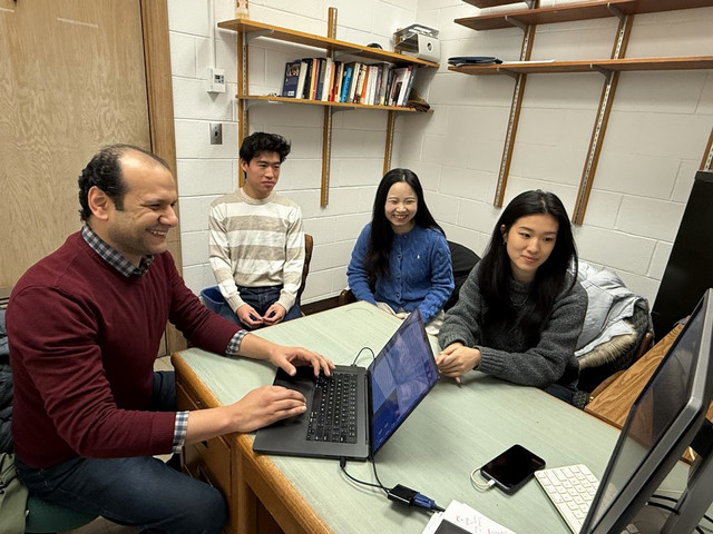 professor and students smiling and looking at computer