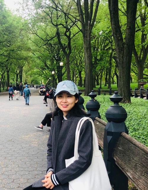 Yan Cong sitting on a bench smiling surrounded by trees