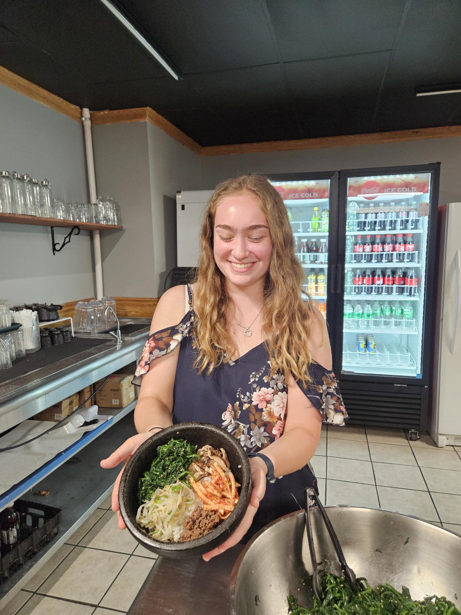 Student holding a prepared bowl of food in a kitchen workspace.