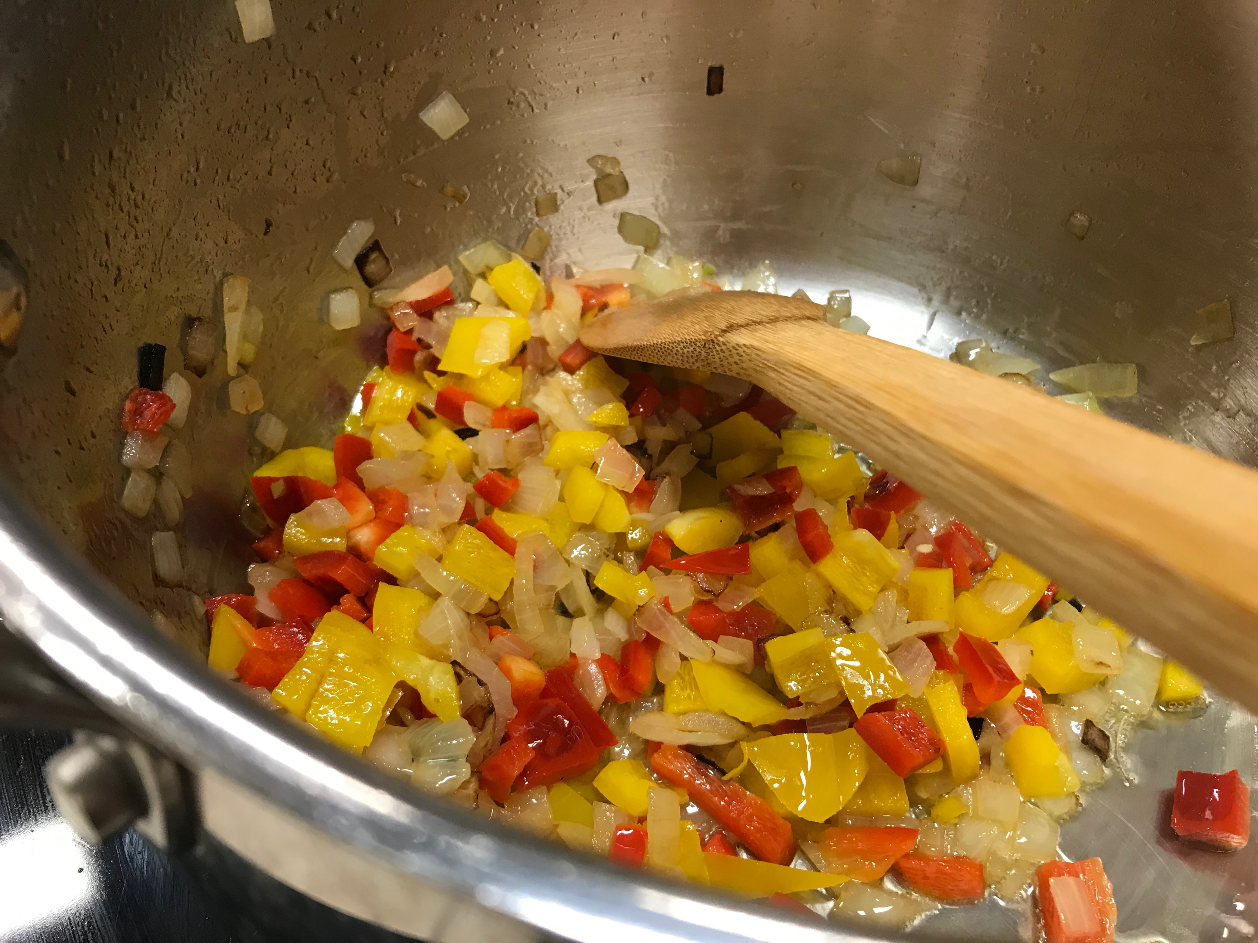 Diced Peppers and Onions Sautéing in a Pot with a Wooden Spoon
