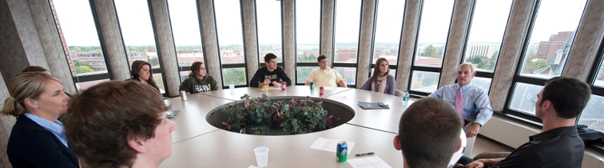 Several CLA alumni sitting around a large round table surrounded by windows in Steven C. Beering Hall of Liberal Arts and Education