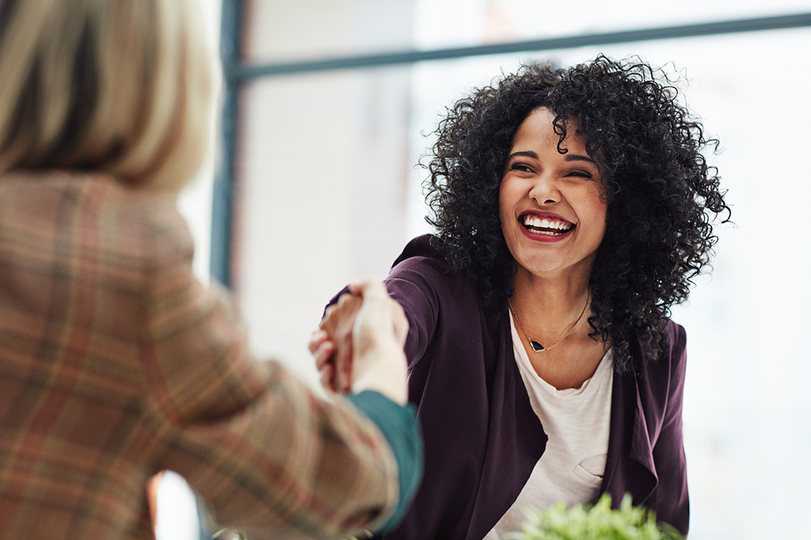 Two women shaking hands while smiling.