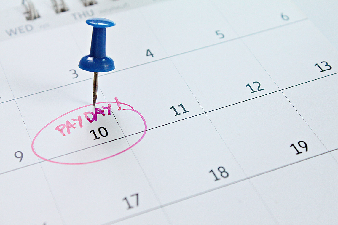 A blue pushpin in a calendar marking the date of pay day.