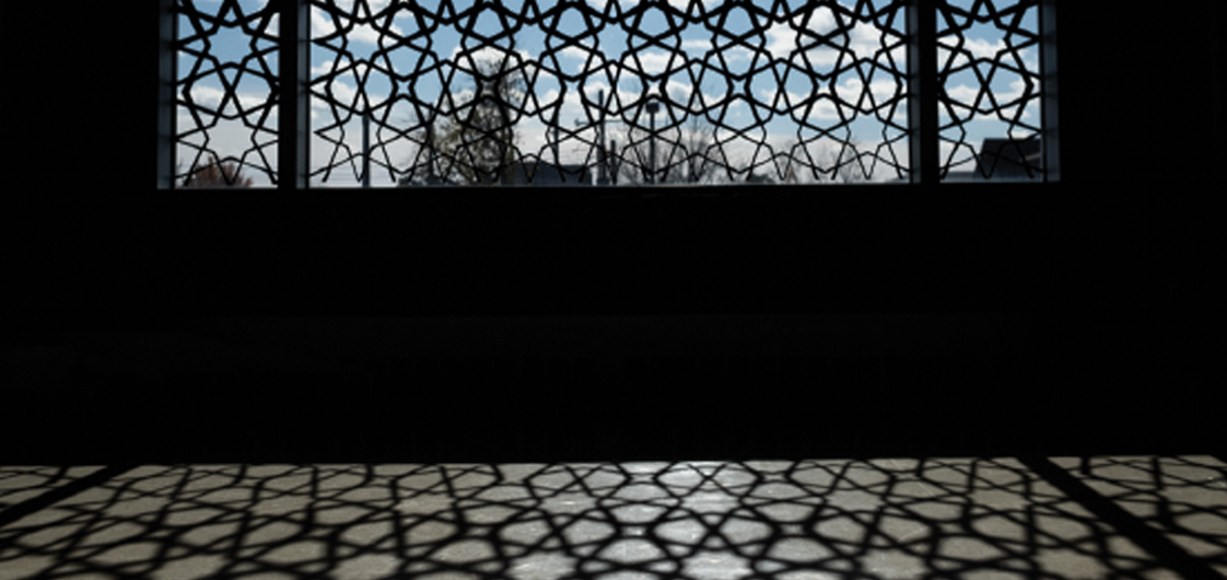 A window with a geometric pattern covering it casting a silhouette. 