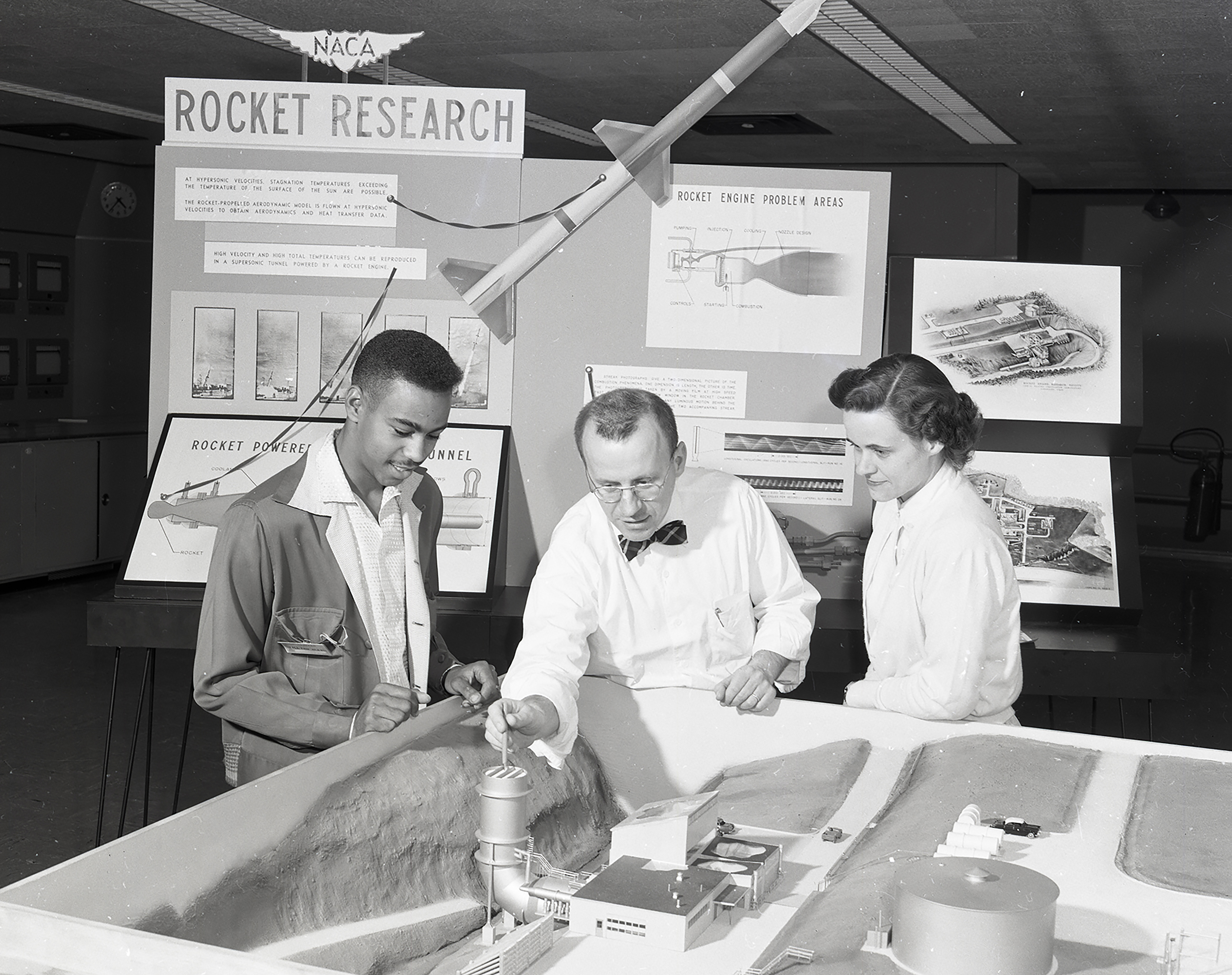 The NACA-Lewis Rocket Research group inspects a model of the new Rocket Engine Test Facility (1957).  Left to right: unidentified student intern, and the two former Zucrow students, Robert Graham, and Elinore Costilow. 
