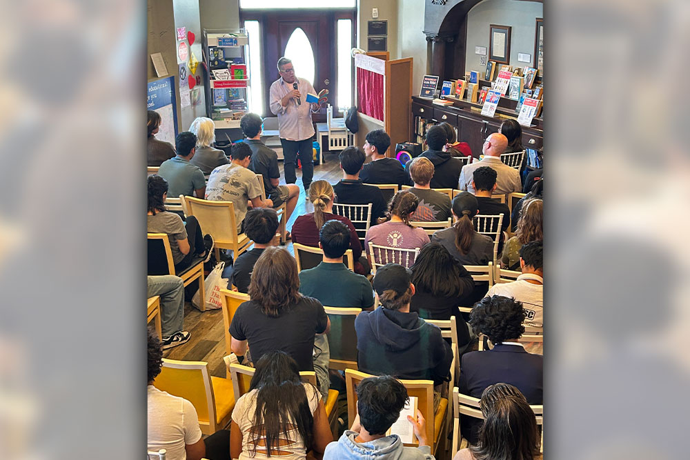 Brian Leung reading from his book while a room-full of students and staff listen.