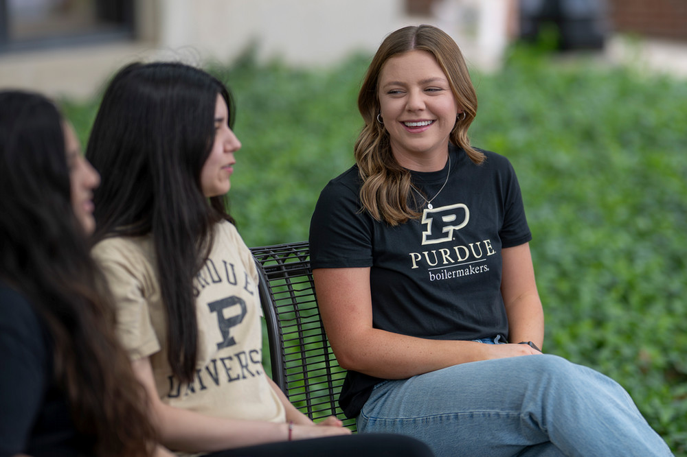 Two Purdue students talking while sitting on a black bench