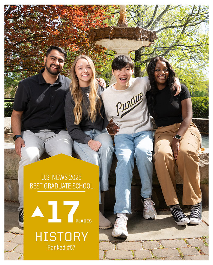 Four students smiling and sitting down by a large water fountain.